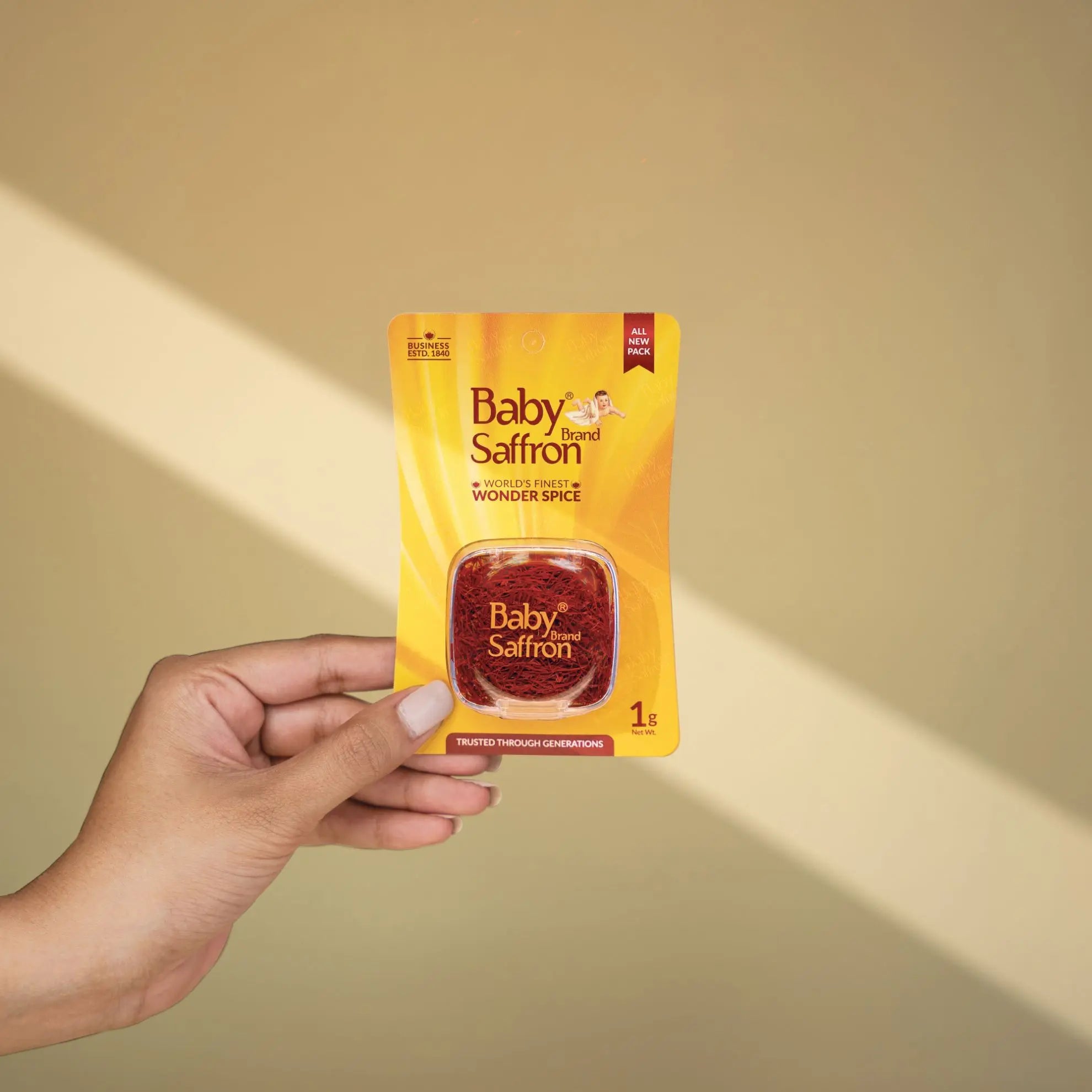 Hand holding a package of Baby Saffron 1gm pack against a beige background