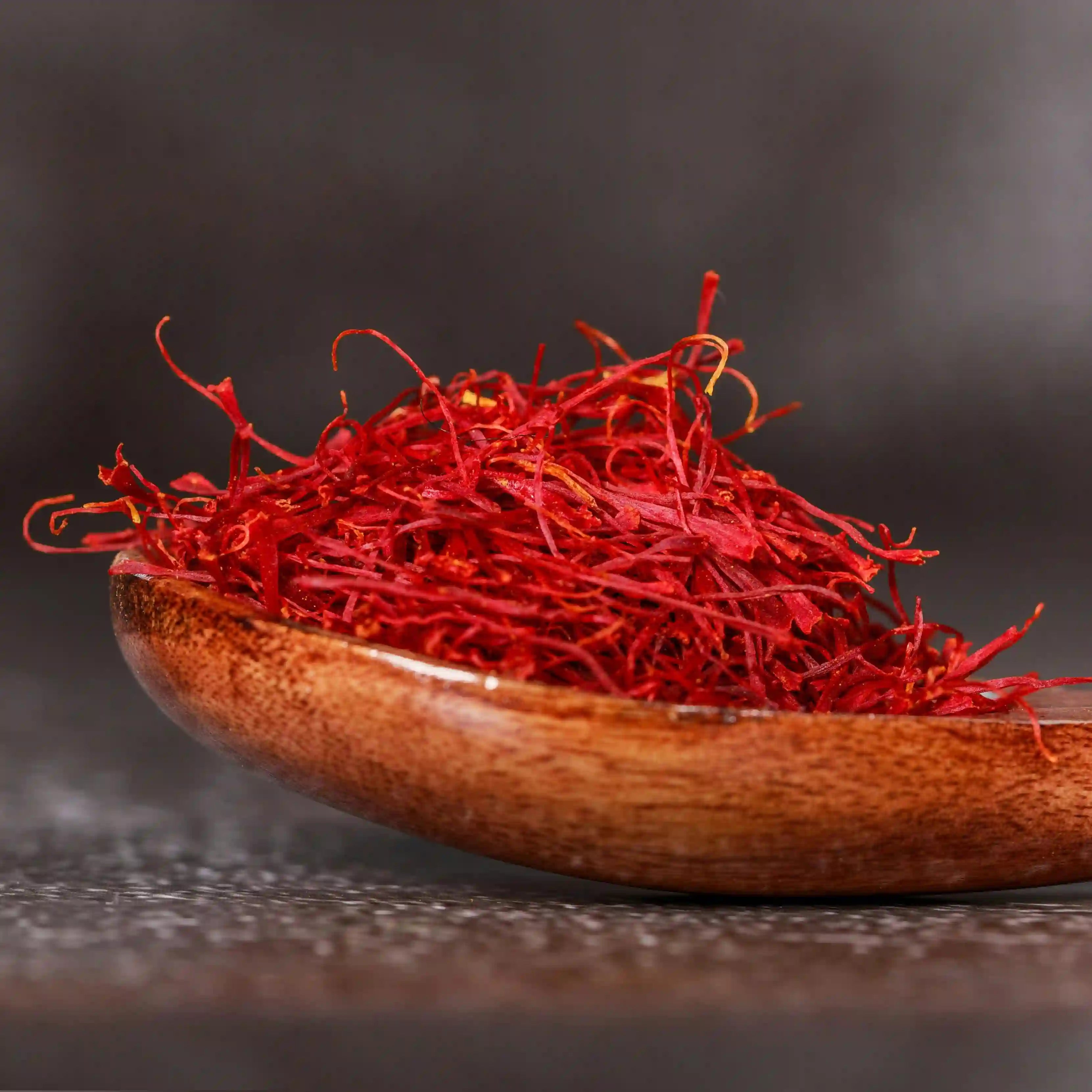 Baby Saffron kesar's long strands on a wooden spoon with a dark background